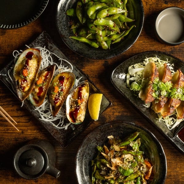 An overhead view of Kase Sake & Sushi appetizers: mussels, edamame, gyoza, and shishito peppers.