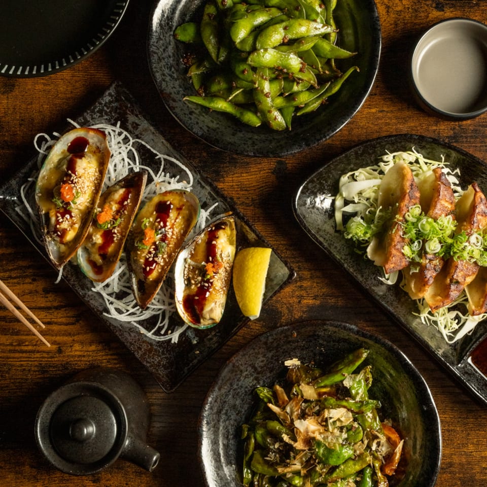 An overhead view of Kase Sake & Sushi appetizers: mussels, edamame, gyoza, and shishito peppers.