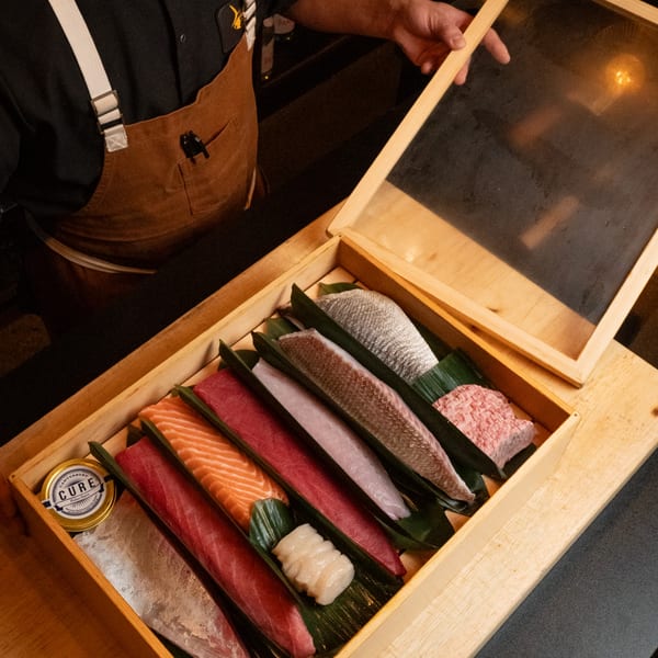 A chef opens a wooden box filled with various cuts of fresh fish and seafood for sushi.