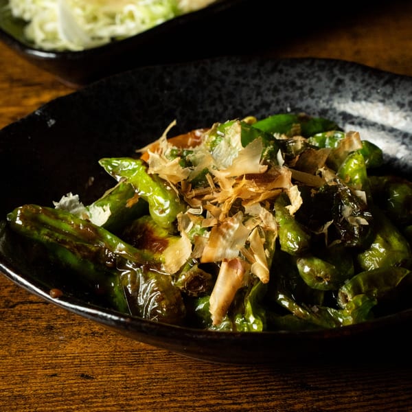 Kase Sake & Sushi's green shishito peppers topped with bonito flakes in a black bowl.