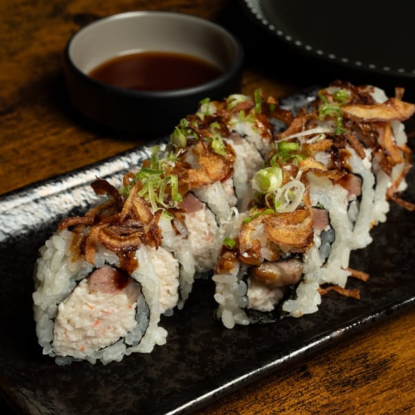 Kase Sake & Sushi's sushi rolls topped with crispy fried onions and green onions, with soy sauce.