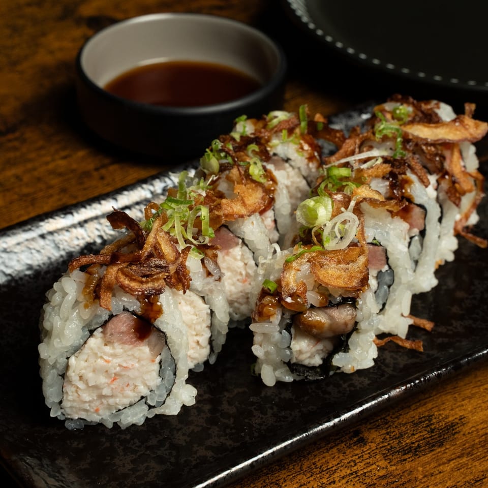 Kase Sake & Sushi's sushi rolls topped with crispy fried onions and green onions, with soy sauce.