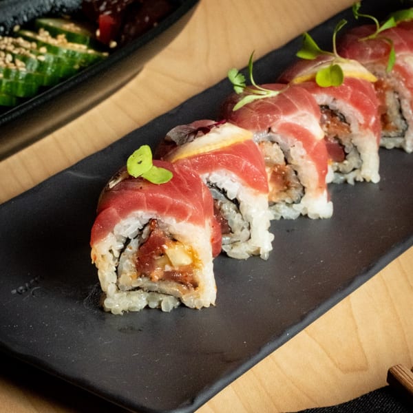 Kase Sake & Sushi's tuna sushi rolls with microgreens and lemon slices on a black plate.